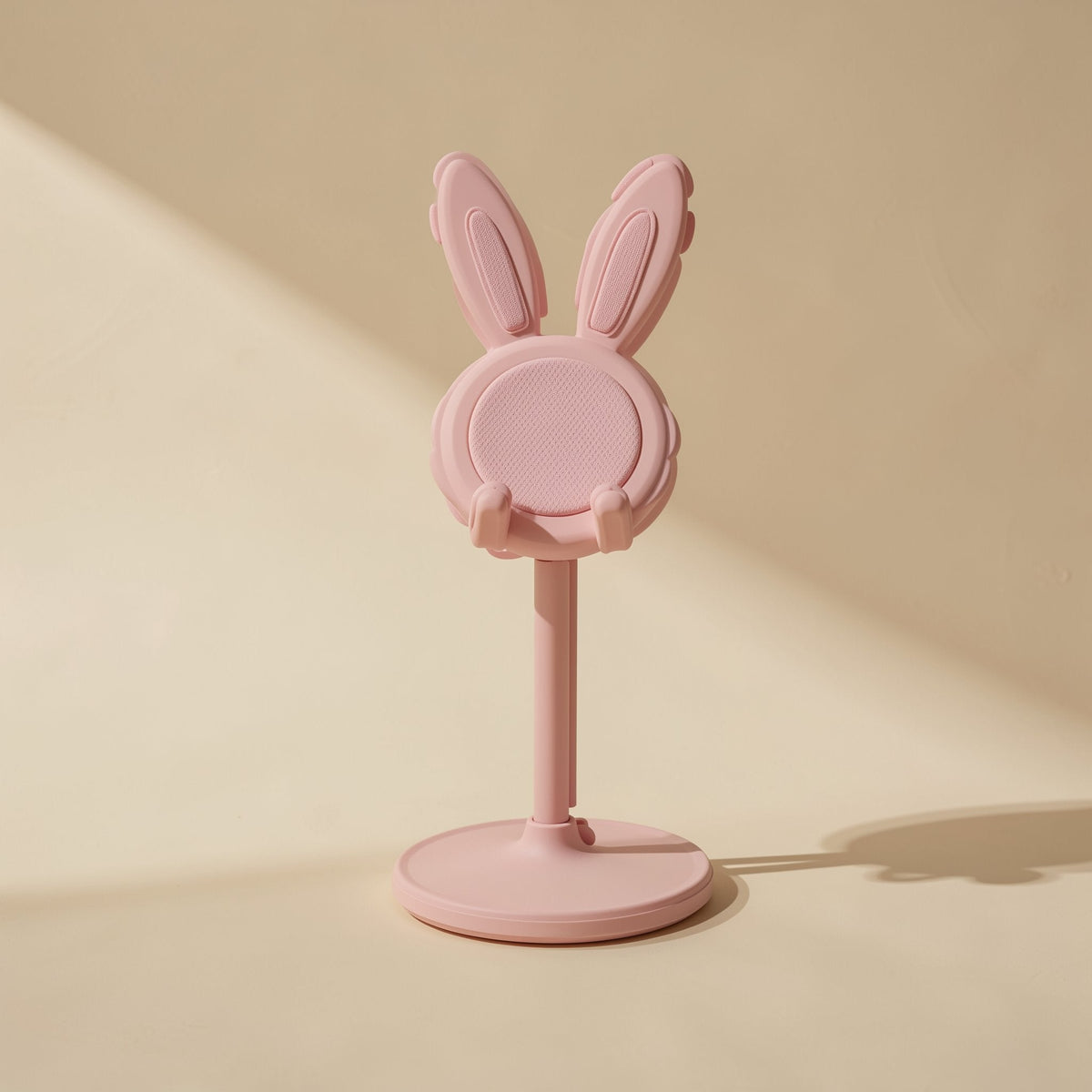 Bunnyrest Rabbit Desktop Phone Stand in pink, front view with long ears on a round base against a cream wall