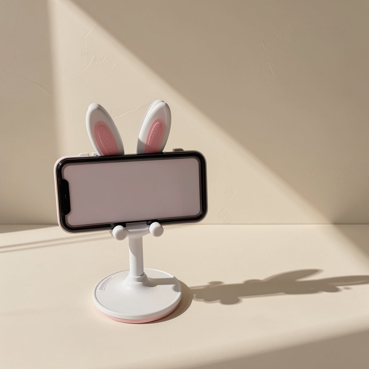 Bunnyrest – White stand with pink inner ears holding a smartphone sideways, small paws gripping the phone's bottom edge