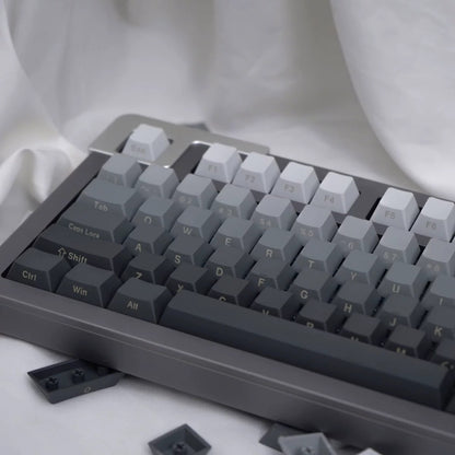 Glasskey – Angled view of grey gradient keycaps on a keyboard with a few loose keycaps resting on white fabric