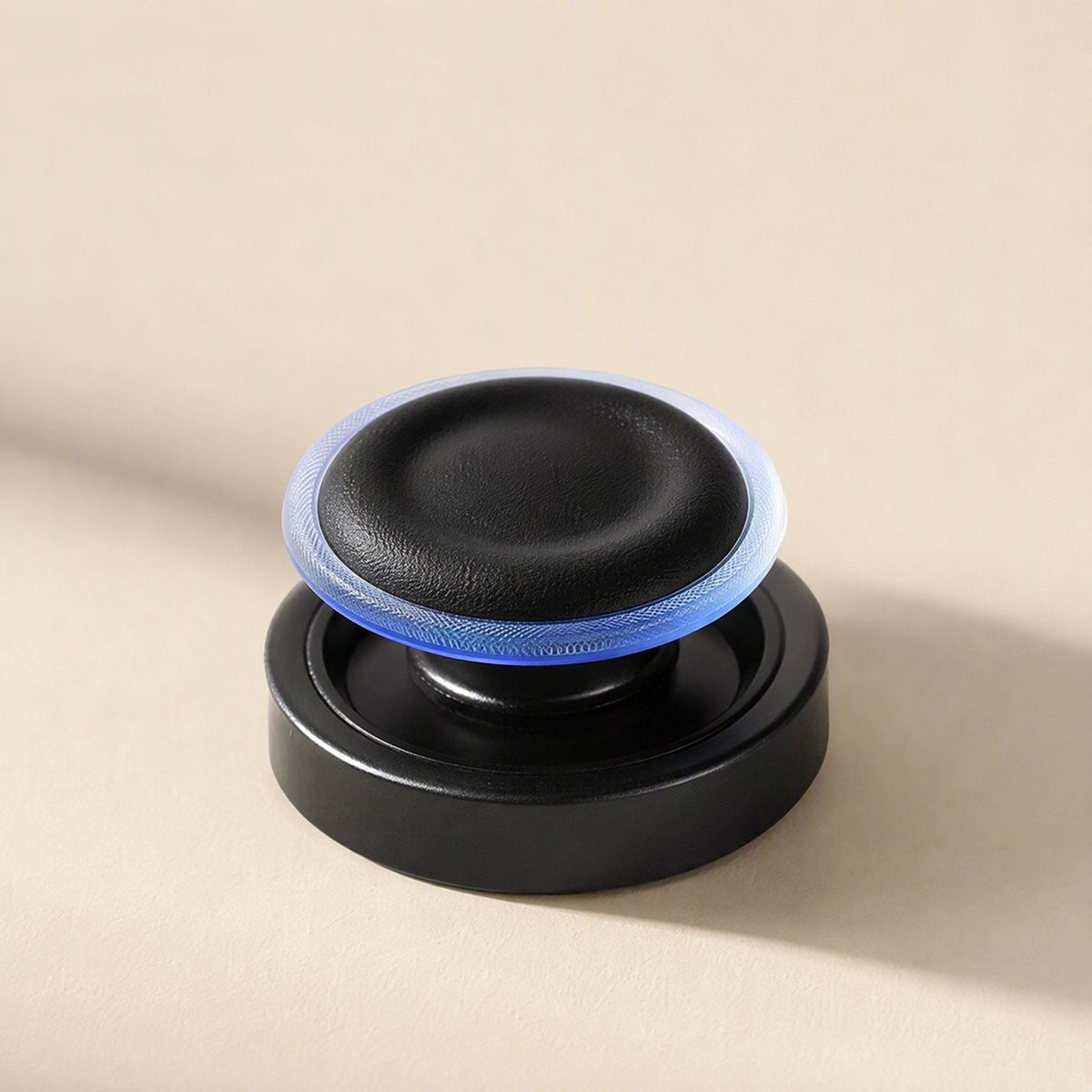 Thumbtread – Black joystick cap with a glowing blue translucent ring, resting on a black base against a cream backdrop