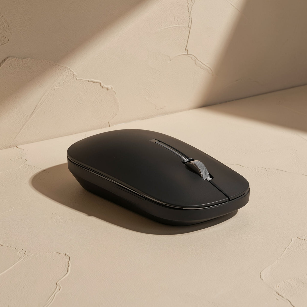 Slimclick – Black low-profile wireless mouse seen from a three-quarter angle on a textured beige surface