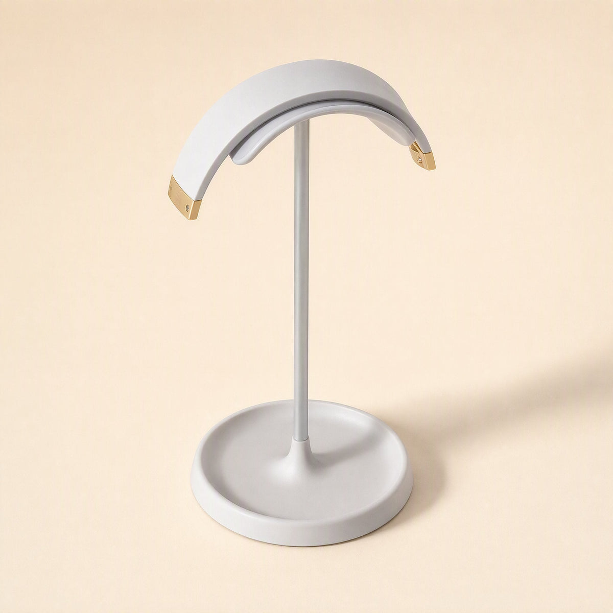 Hookrest Metal Desktop Headphone Stand in white with gold-tipped ends on a round tray base, three-quarter view