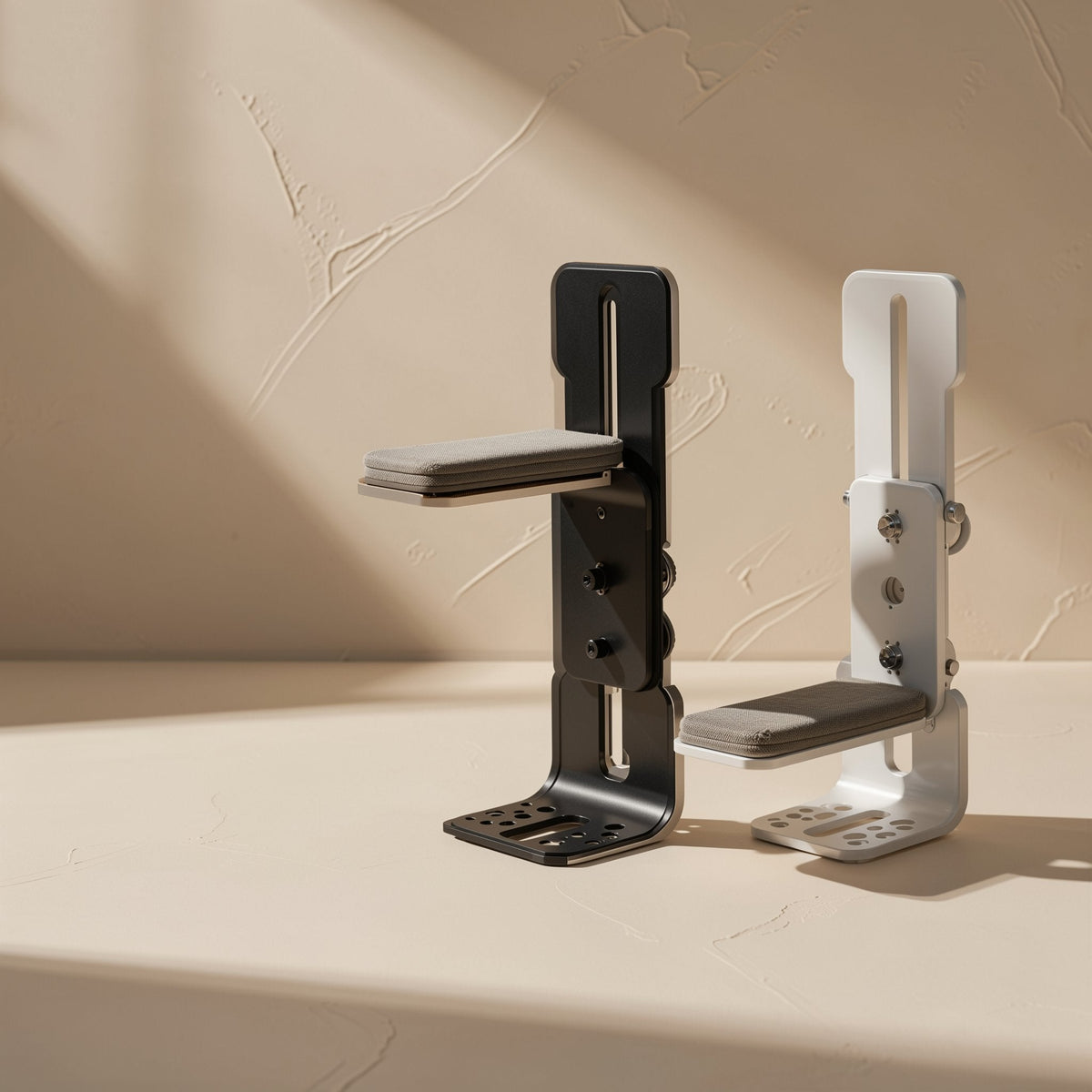 Anglehold – Black and white L-shaped brackets side by side, each with a padded support arm and perforated base plate