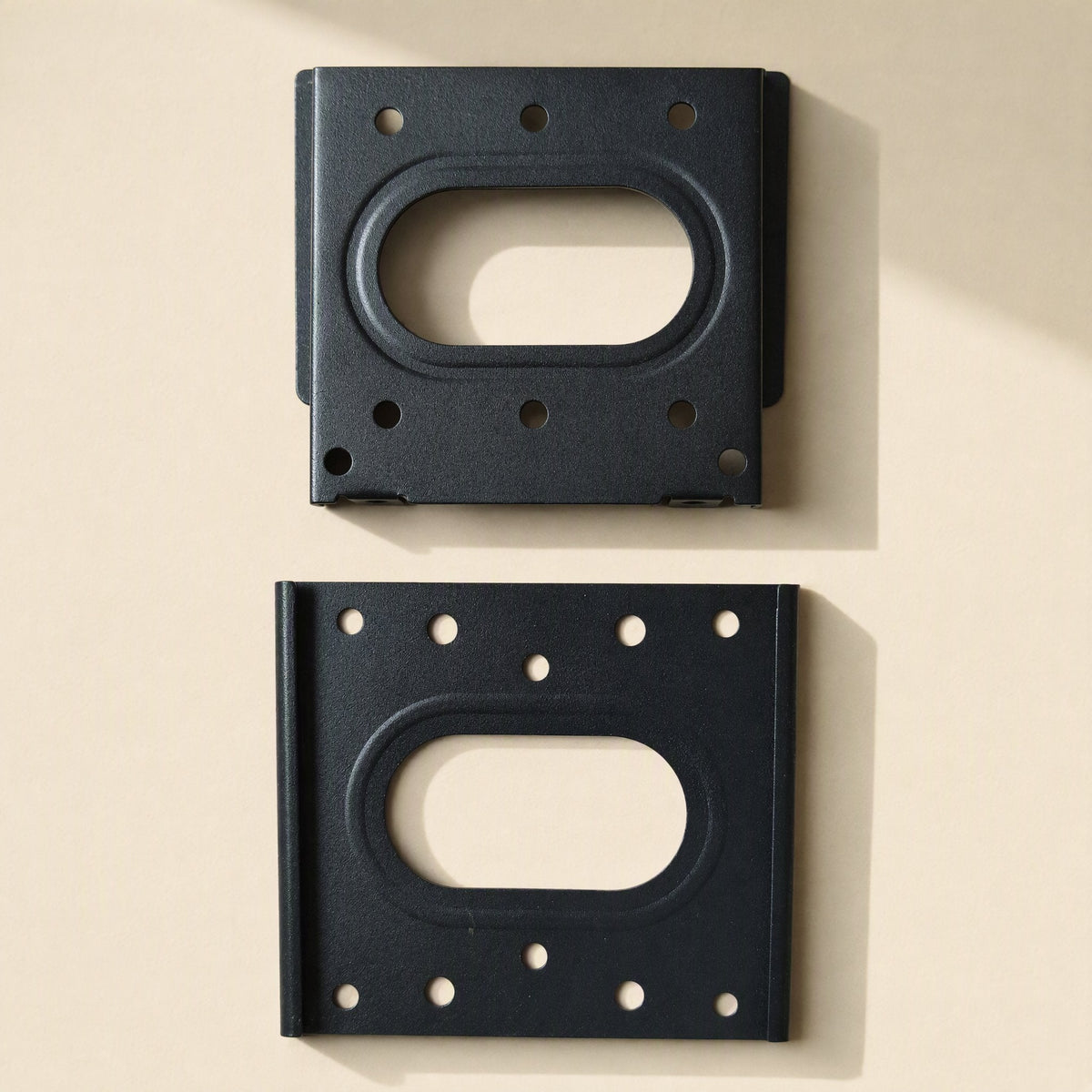 Walllock – Two black bracket plates shown from above, one with raised edges and one flat, each with an oval cutout