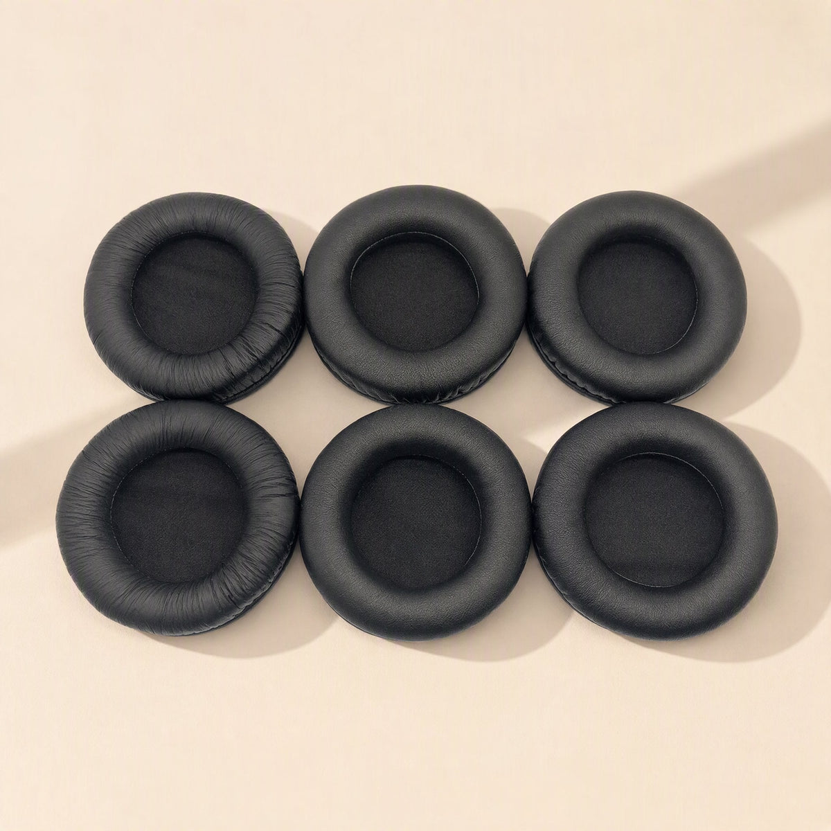 Earcush – Six black earpads arranged in two rows of three on a cream background, seen from above