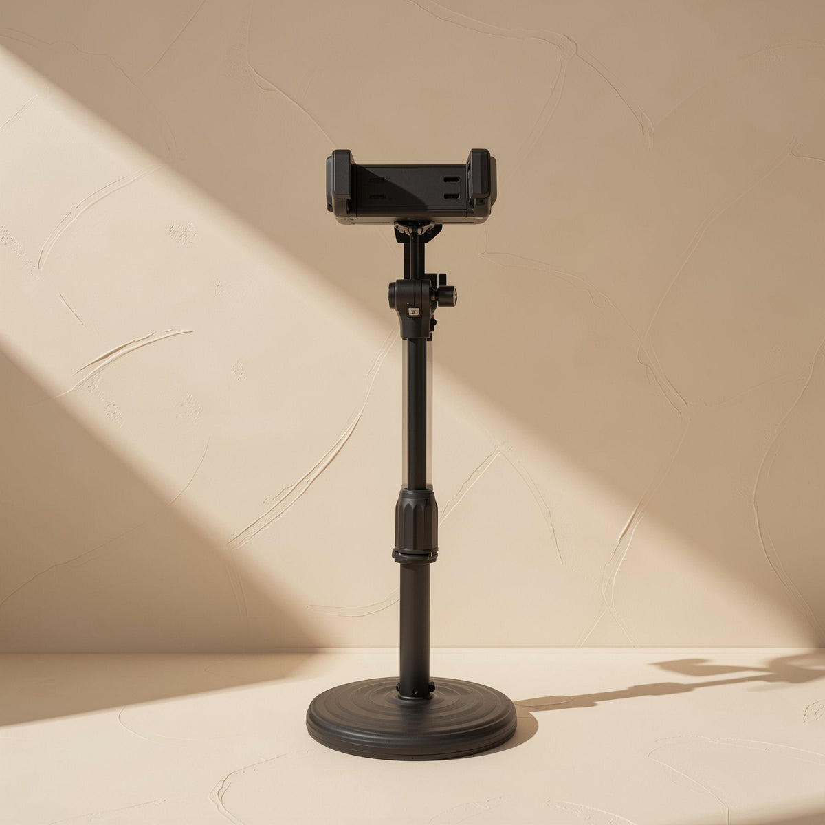 Tiltperch – Black telescopic desktop phone stand with an empty clamp, extended on a round base against a beige wall