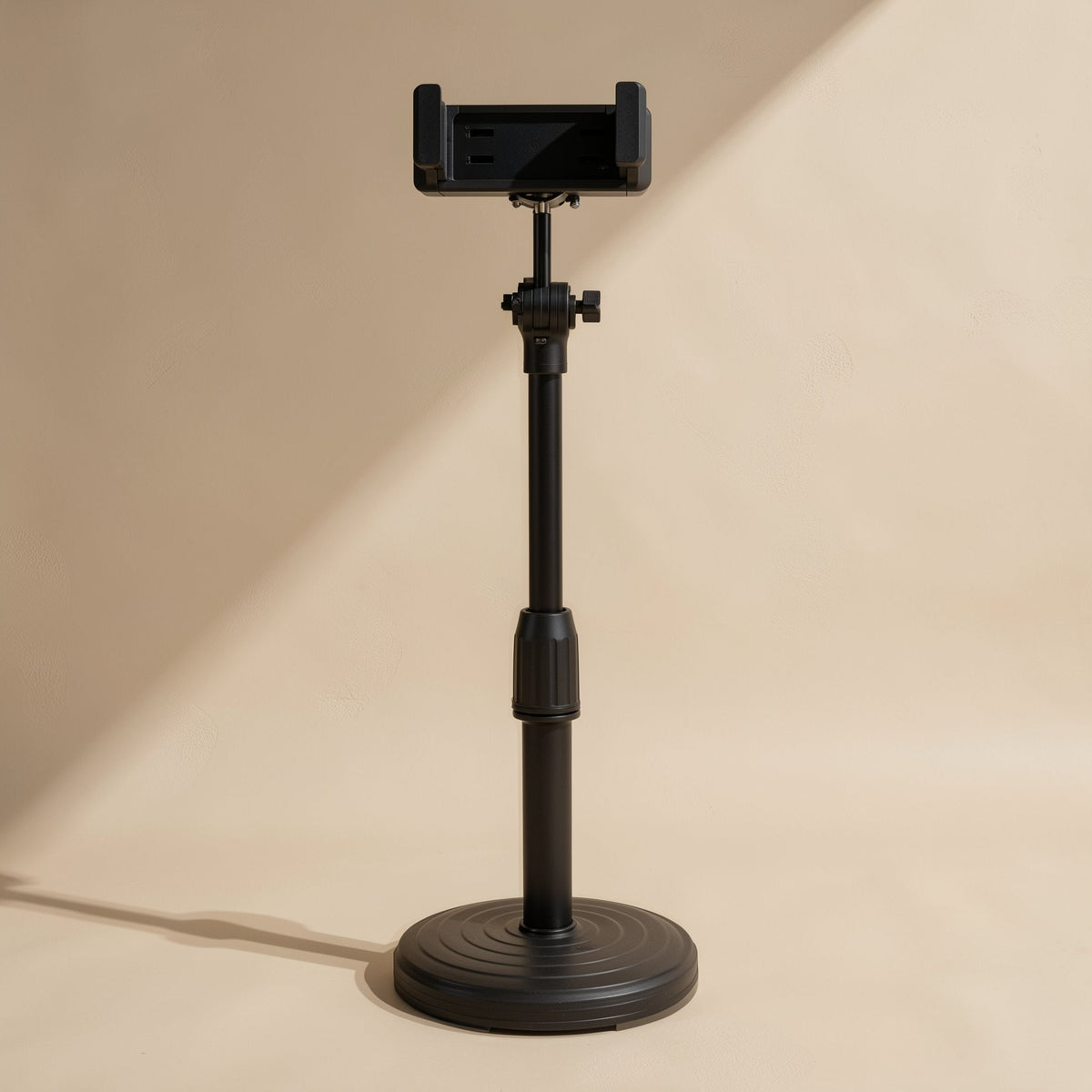 Tiltperch – Black phone stand fully extended with a tall pole and ribbed round base, empty clamp at top, beige backdrop