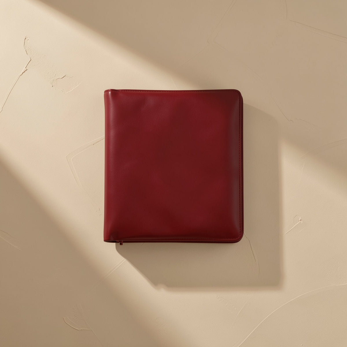Voltrest 15W Qi Wireless Charger – burgundy leather zip-around case with a smooth finish on a sand-colored textured surface