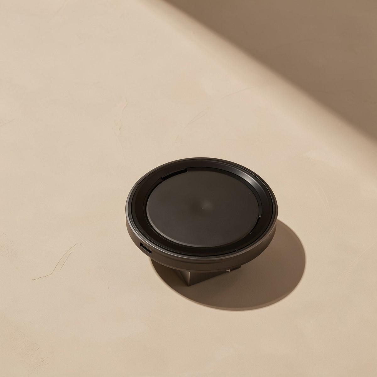 Voltrest – Round black wireless charger angled on a beige surface with a side port and a small plug underneath