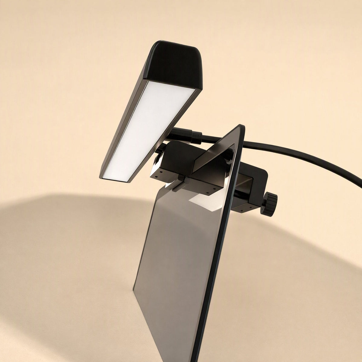 Usbglow – Black clip-on light bar angled above a monitor's top edge, with a black cable and thumbscrew on the clamp