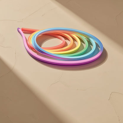 Neonflex – Neon light strip in a loose teardrop coil glowing red, yellow, green, blue and pink on a tan surface