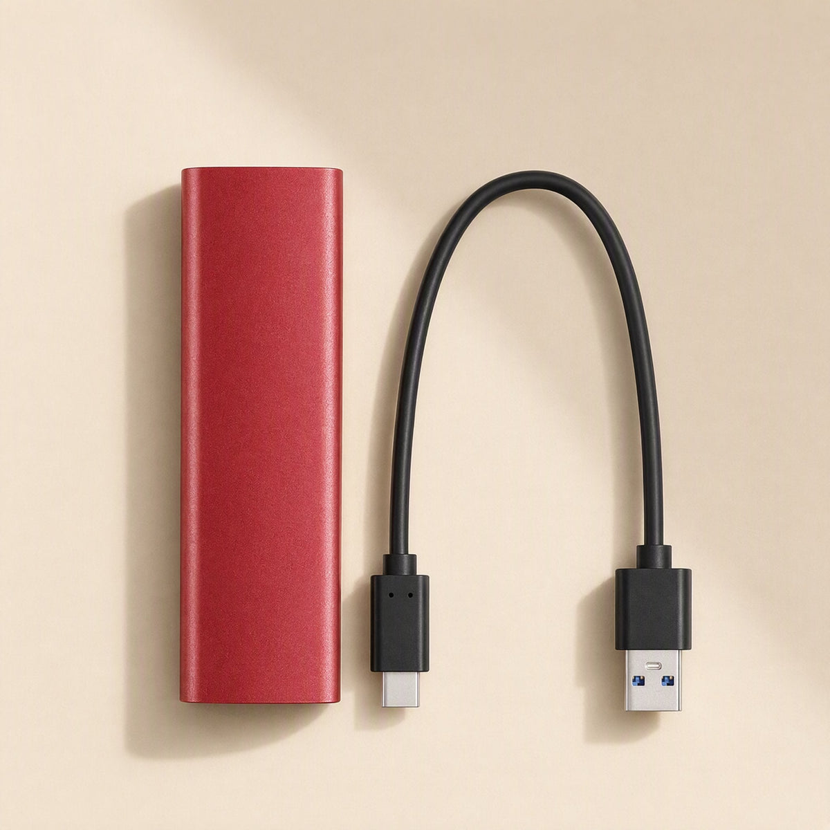 Steeldisk Metal Shell Solid State Drive – red metal SSD beside a black USB-C to USB-A cable on a cream surface, top-down view