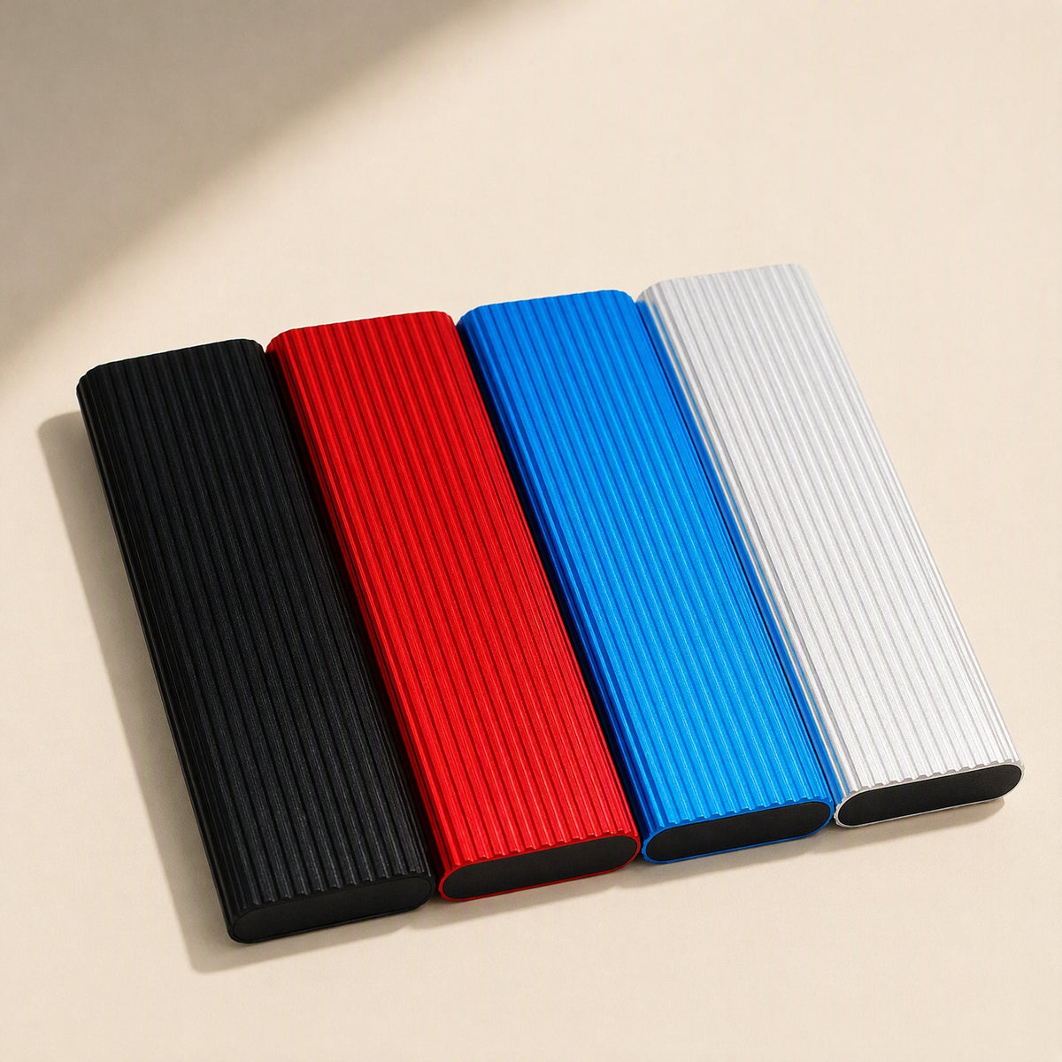 Driveswift – Four ribbed metal portable drives in black, red, blue and silver lying flat on a cream surface