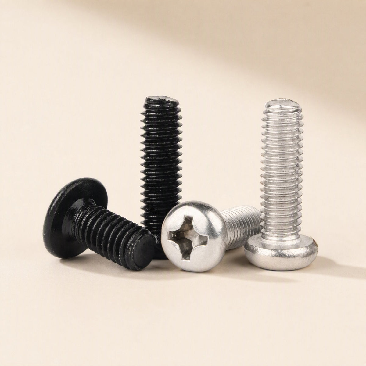 Flatfix – Black flat-head screw and two silver pan-head Phillips screws, with threads shown, on a beige surface