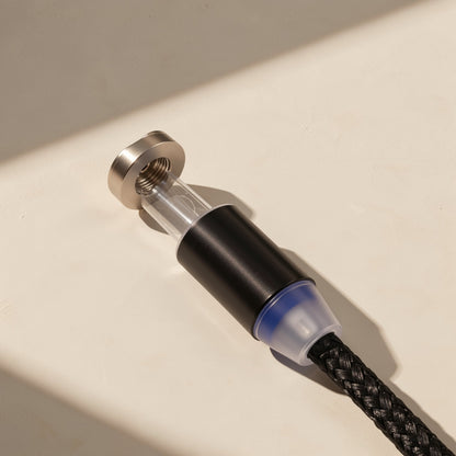 Magtrio – Black magnetic cable head with clear section, blue-tinted collar and threaded metal end, on a cream surface