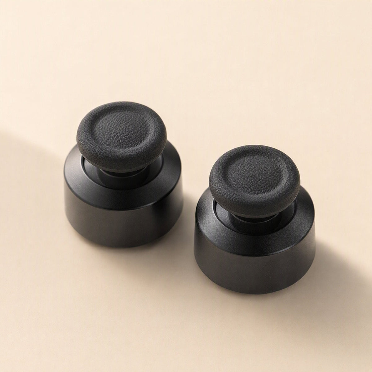 Stickgrip – Pair of black aluminum thumbstick bases with textured grip tops on a cream background