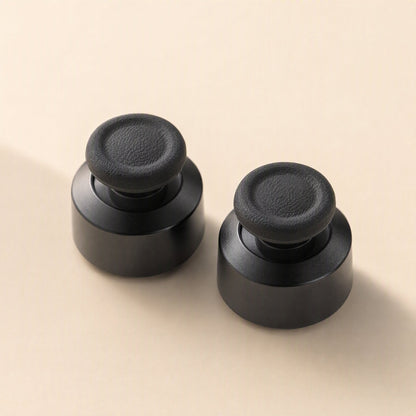 Stickgrip – Pair of black aluminum thumbstick bases with textured grip tops on a cream background