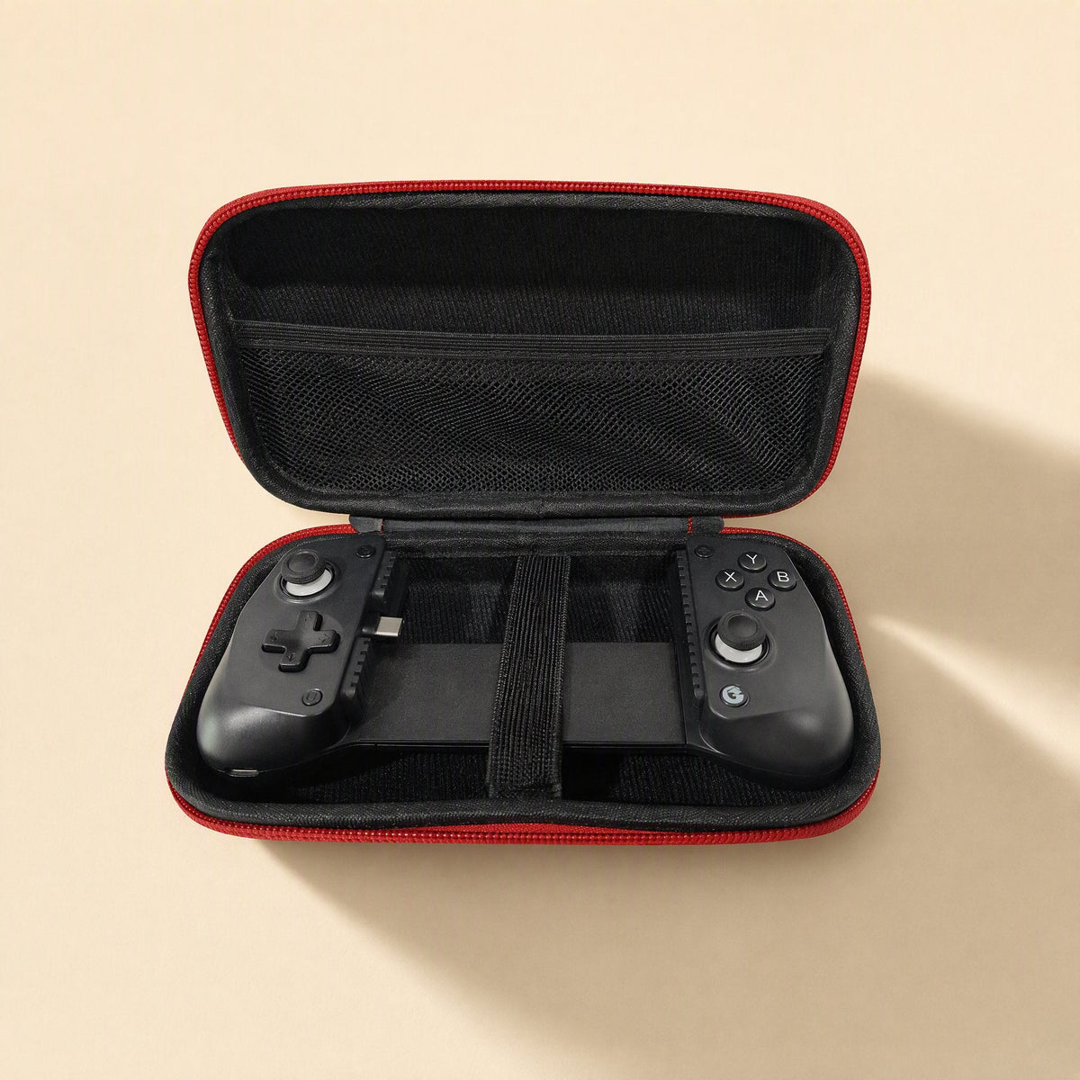 Padpouch – Open black case with red trim, mesh lid pocket and elastic strap holding a mobile game controller