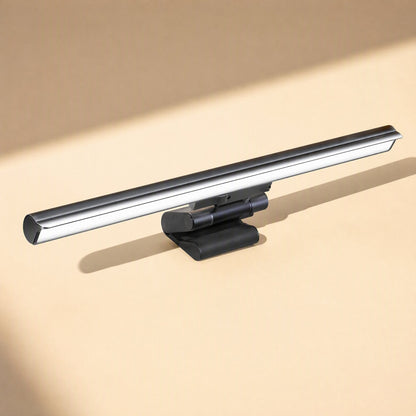 Hangglow – Black monitor light bar with a rounded clip base, seen from a low angle against a warm beige backdrop