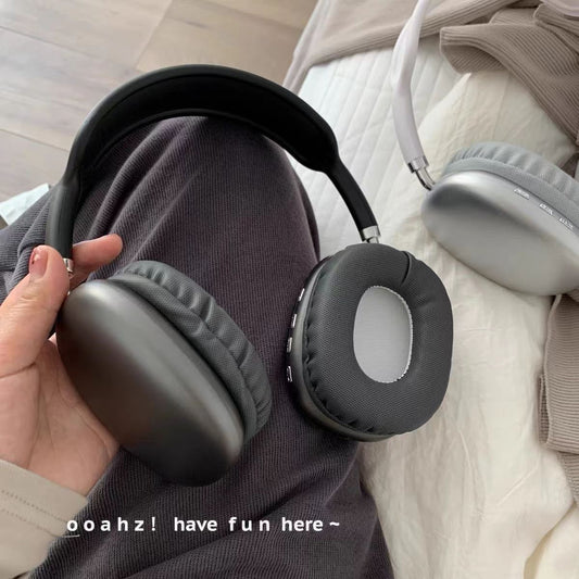 Airsound – Black headphones held in hand over grey trousers, with side buttons on the ear cushion and a white pair behind