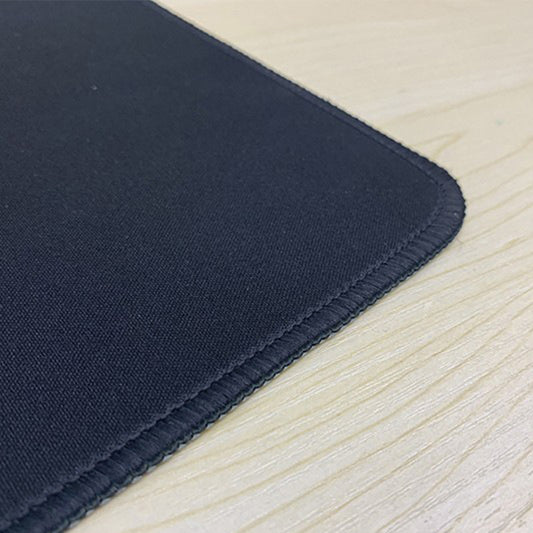 Stitchgrip Cloth Mouse Pad – close-up of a black mouse pad's rounded corner with stitched edge on a light wood desk