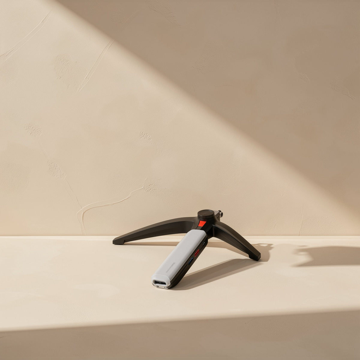 Portlink – Slim silver and black hub standing upright on a small black tripod stand against a beige wall