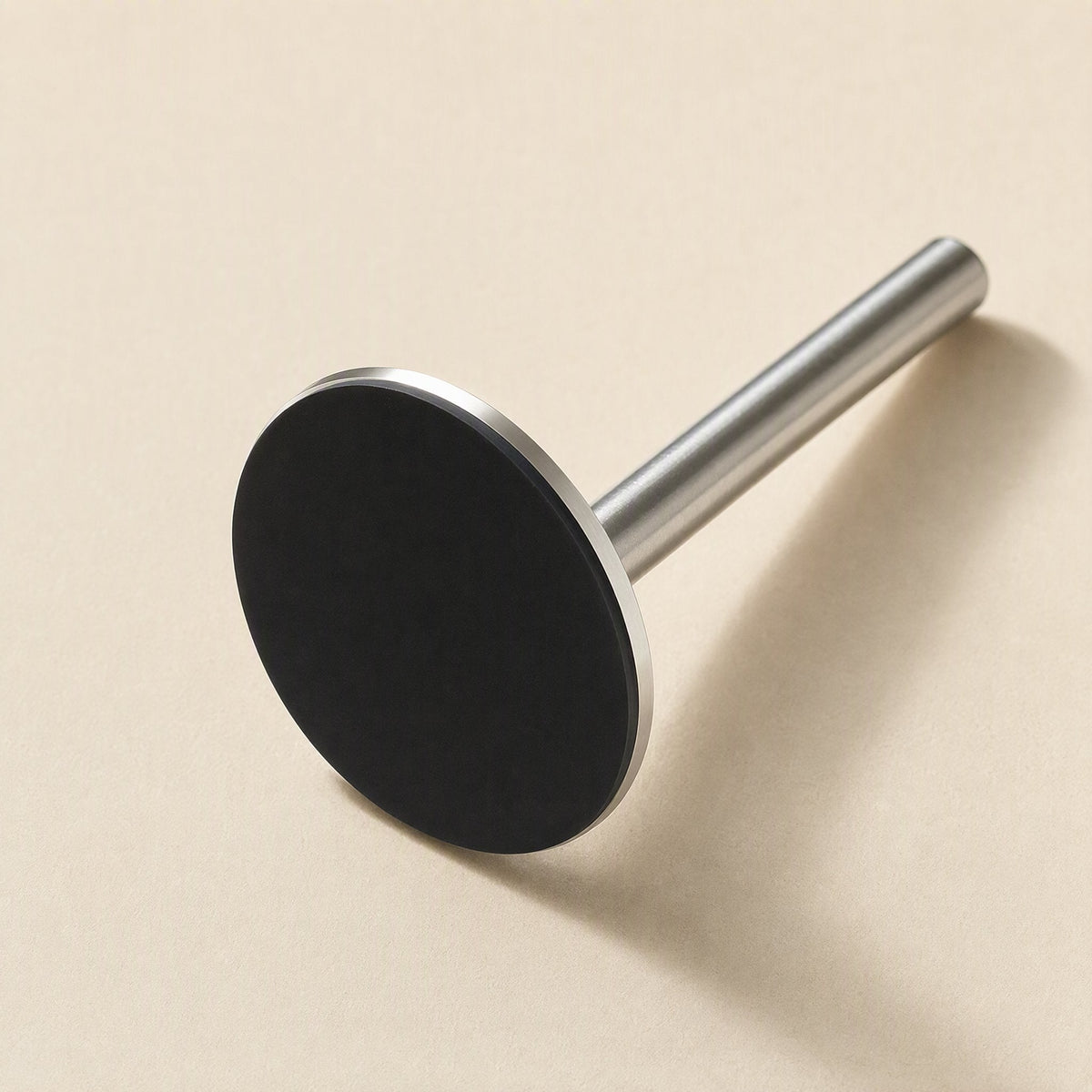 Magbrace – Round black magnetic base disc attached to a short silver post, angled view on a cream surface