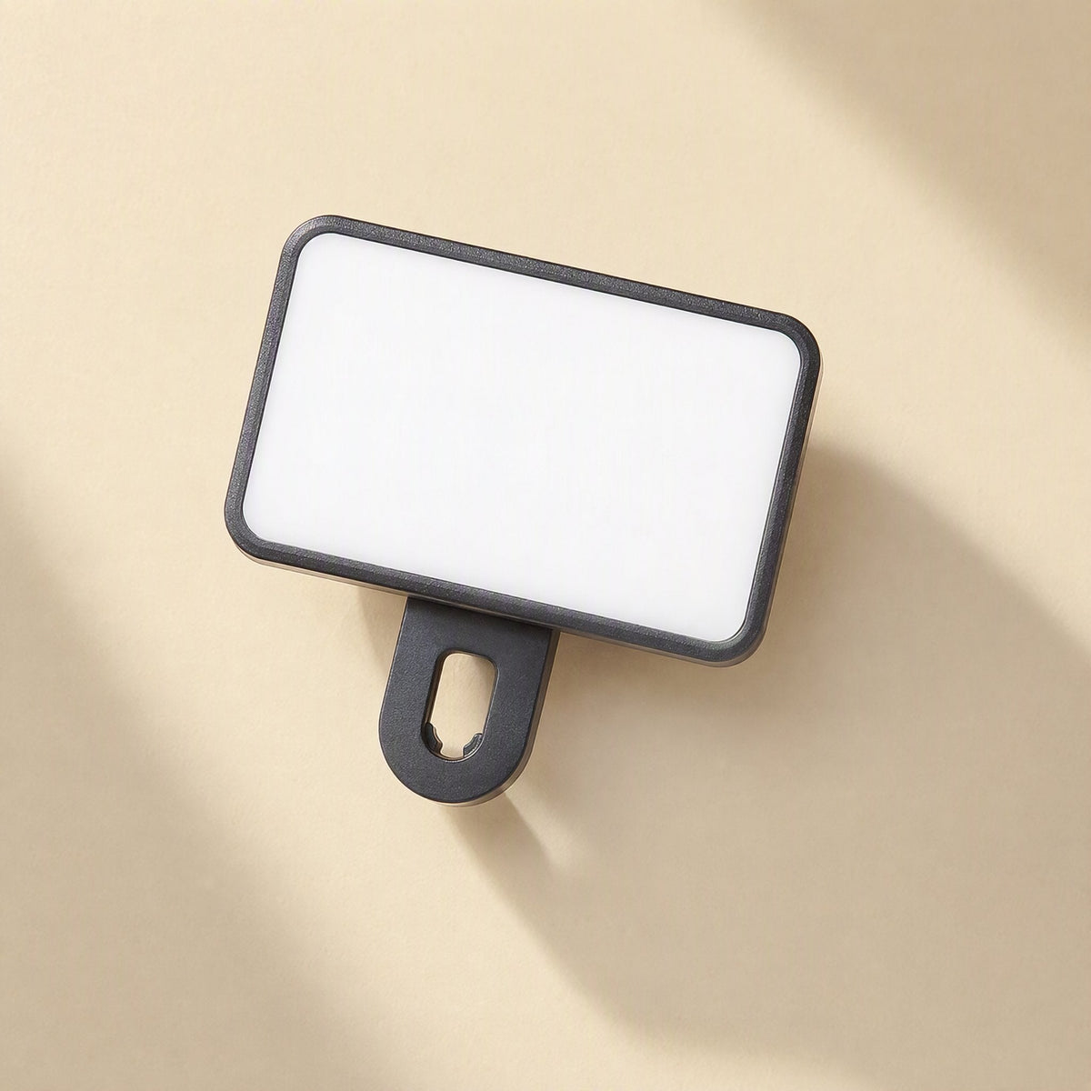 Snapshine Clip-On Phone Photography Fill Light, black rectangular panel with a slotted clip, top-down on beige