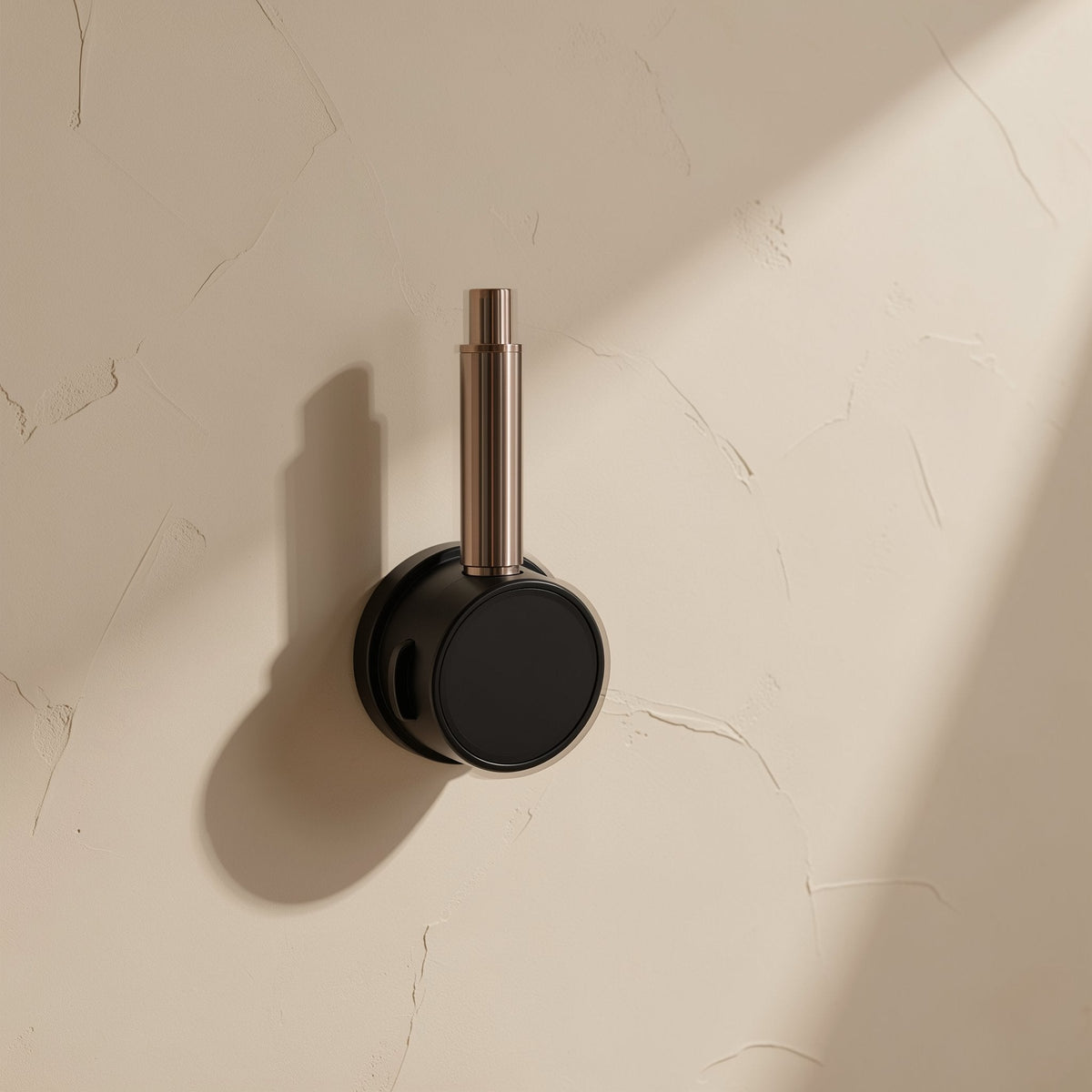 Spinloop – Black and copper-toned cable holder with a slim post, mounted on a beige wall