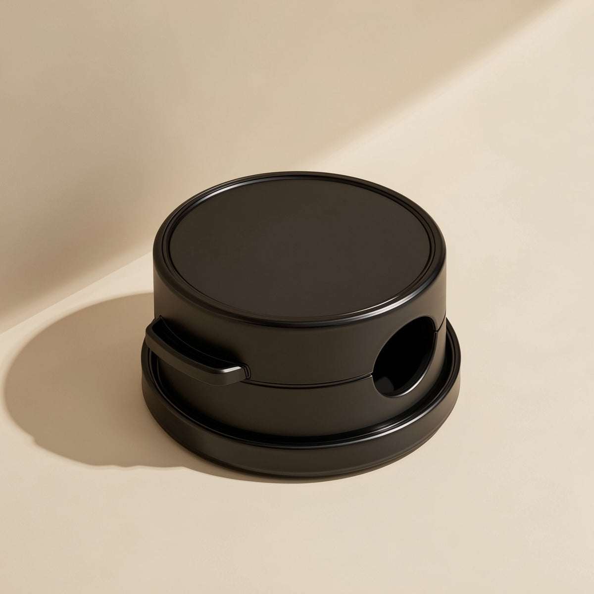 Spinloop – Black cylindrical cable organizer with side opening and handle, three-quarter view on a beige background