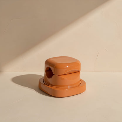 Spinsteady Rotating Charging Cable Organizer in glossy terracotta orange on a cream surface with shadow
