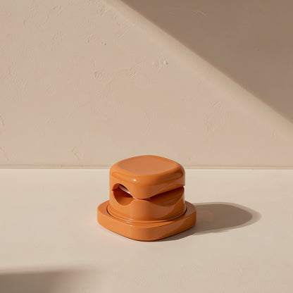 Spinsteady – Glossy terracotta organizer seen straight on, showing the two cable slots in its rounded stacked body