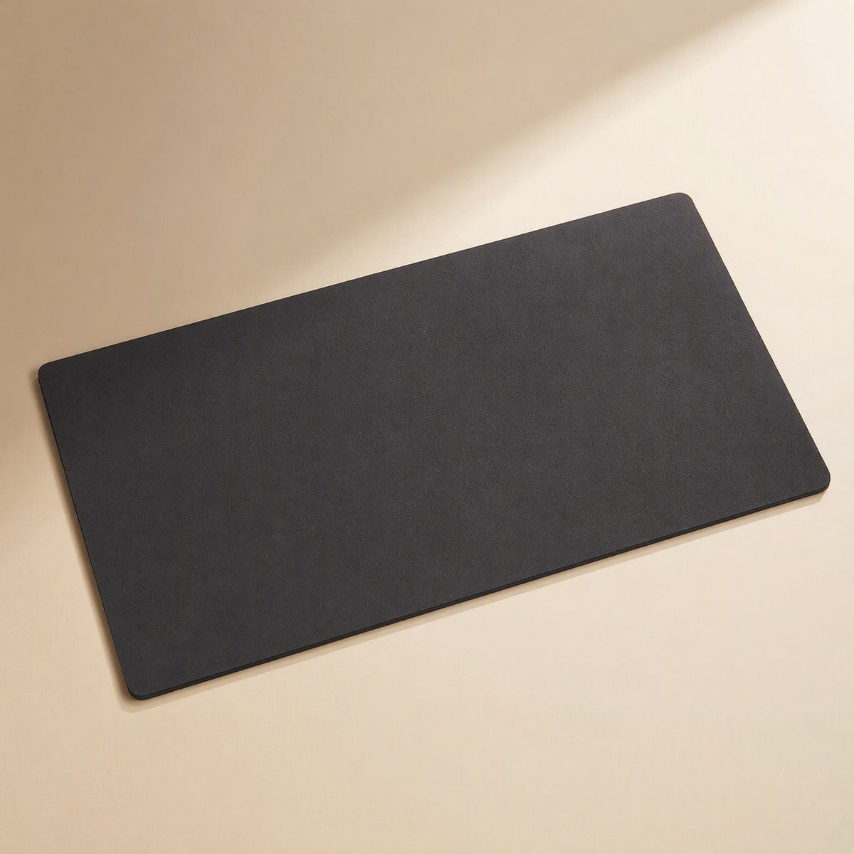 Smoothpad PU Leather Desk Mat in black, shown at an angle on a cream surface with soft light
