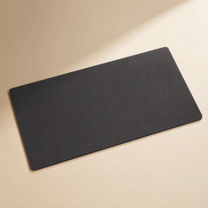 Smoothpad PU Leather Desk Mat in black, shown at an angle on a cream surface with soft light