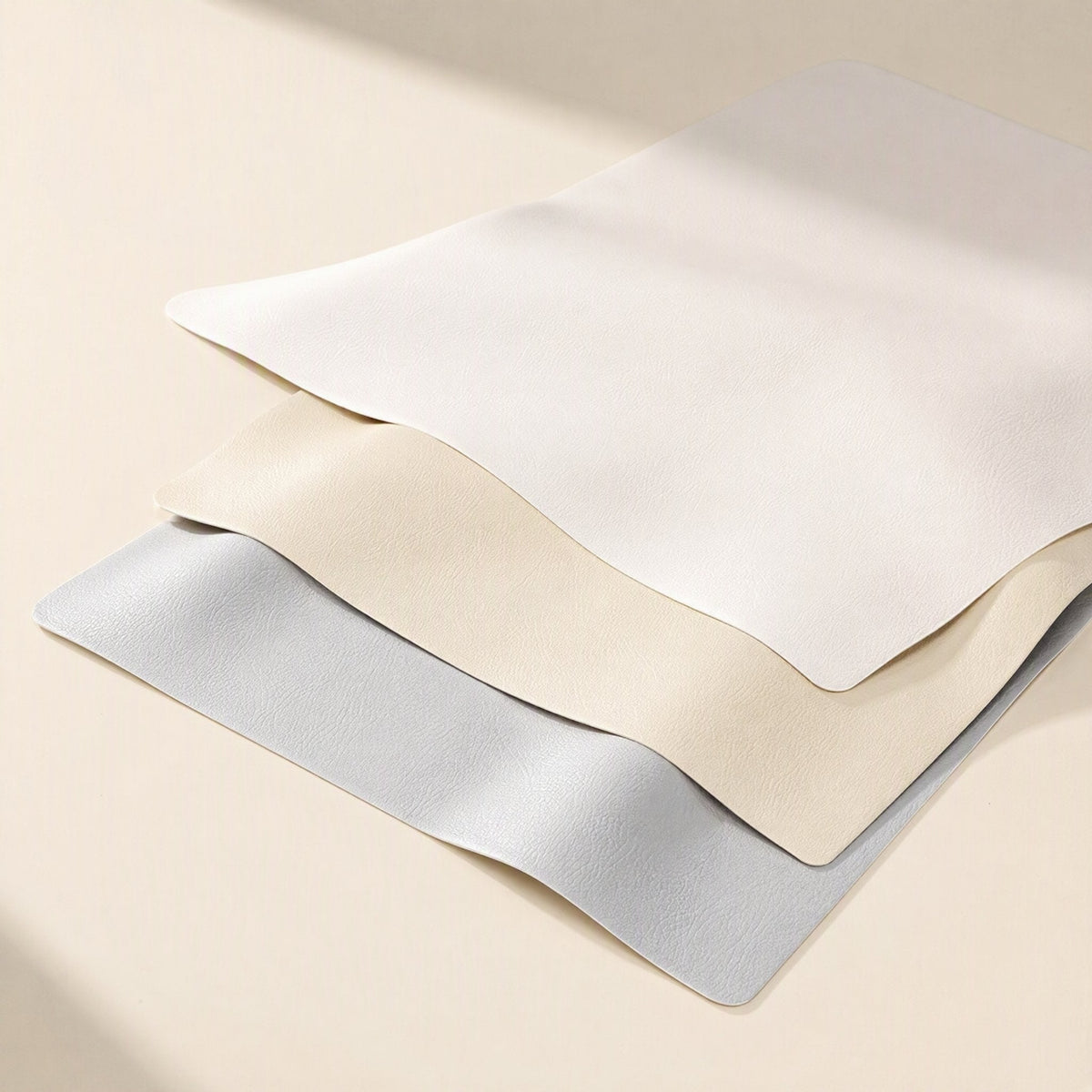 Smoothpad PU Leather Desk Mat – three desk mats in white, beige and light blue-grey stacked with gently waving edges