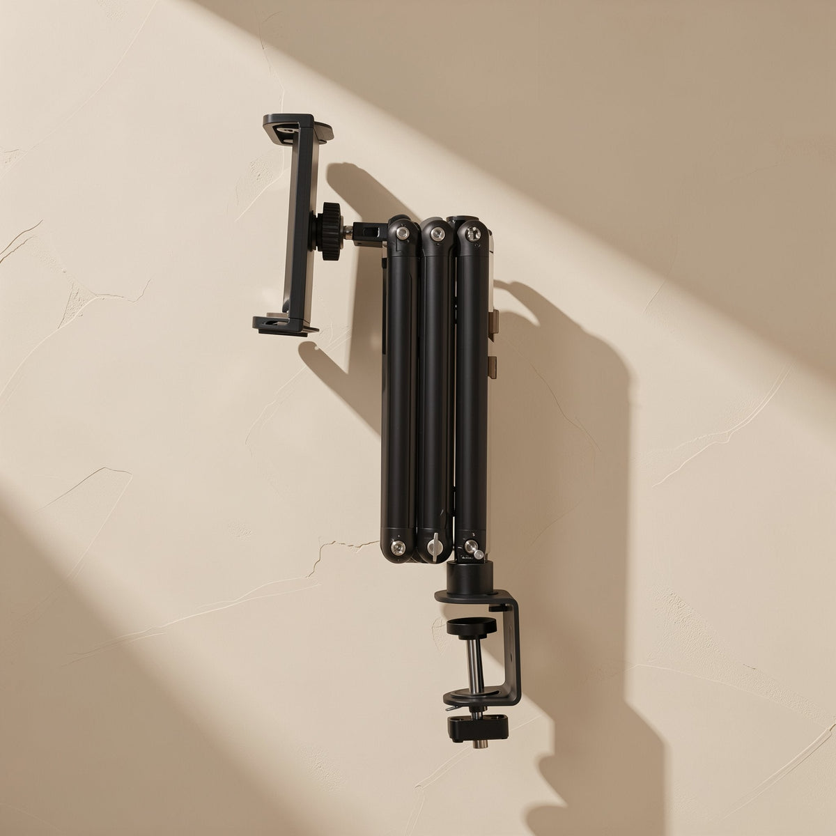 Foldvoice – Black folded arm clamped to a desk edge with an empty tablet holder, seen from the front against a wall