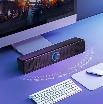Humline USB-powered desktop speaker with glowing blue ring knob on a desk below a monitor, beside a keyboard