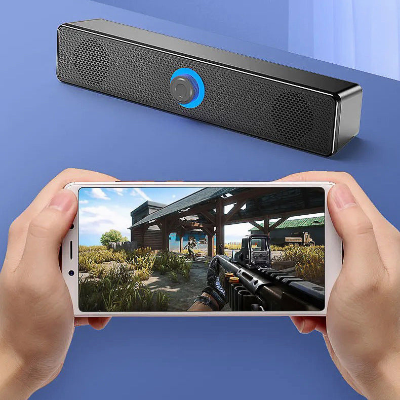 Humline USB-Powered Desktop Speaker – slim speaker bar with blue ring knob above hands holding a phone showing a shooter game