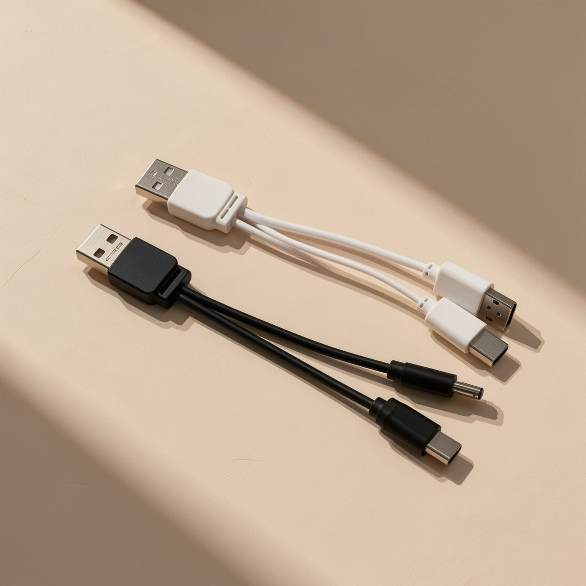 Typepair – White and black USB splitter cables with differing tips, one with a round barrel plug, on a cream backdrop