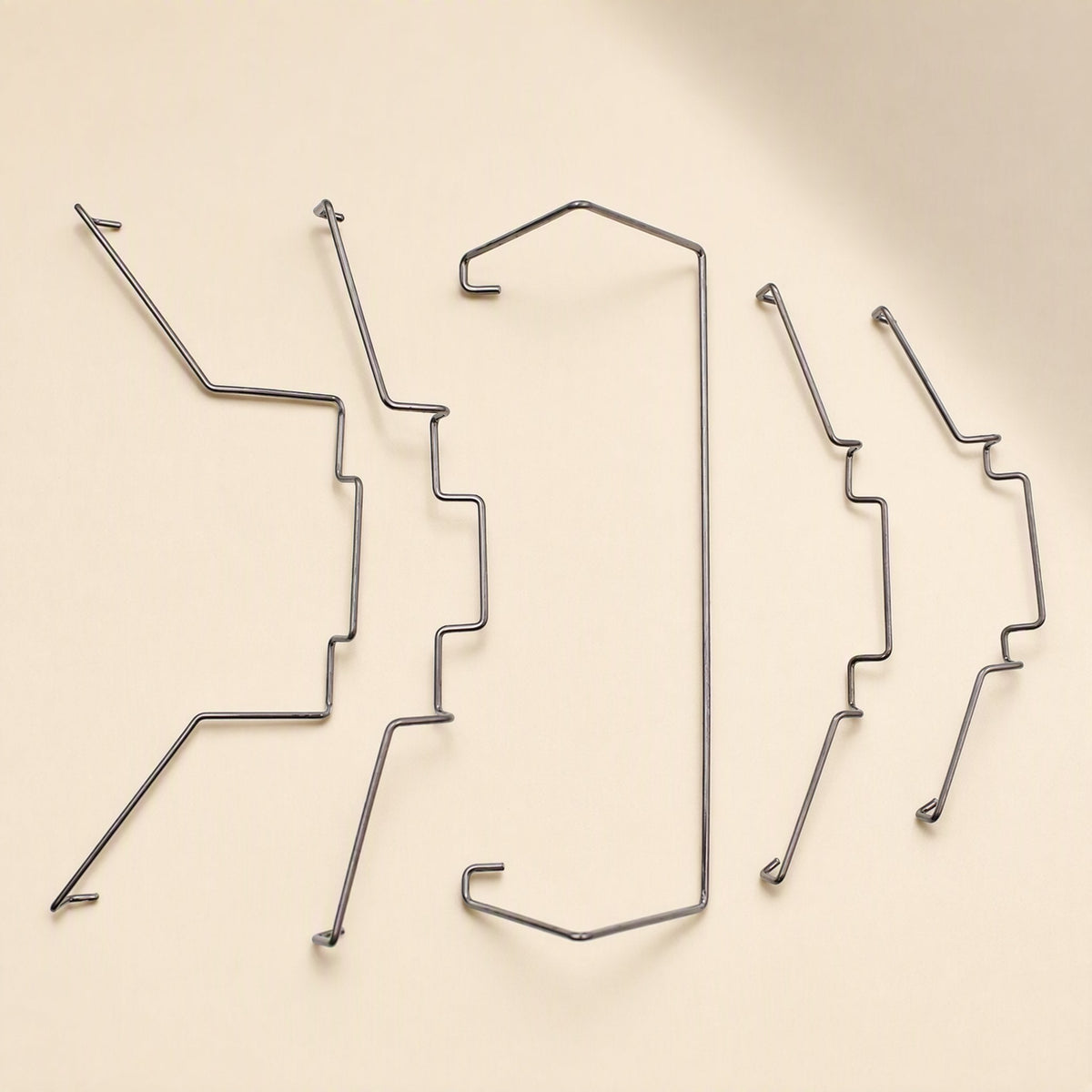 Fanclip – Five bent steel wire fan clips in two sizes arranged in a row on a beige surface, angled view