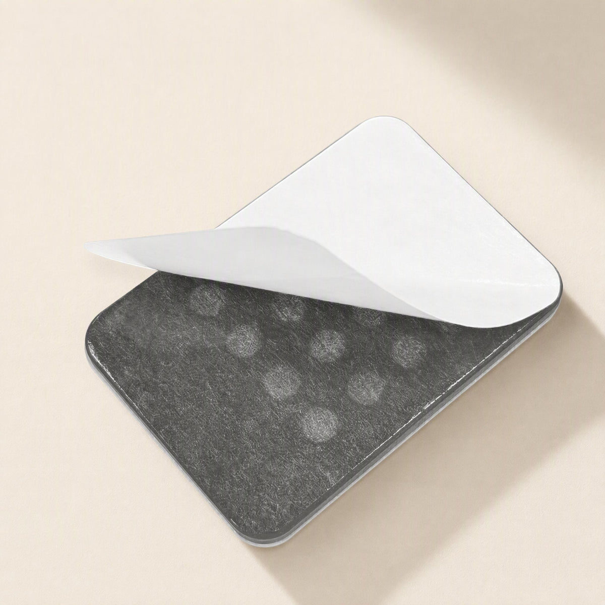 Suctionstay – Back of a grey phone holder with the white adhesive backing peeling away from one corner