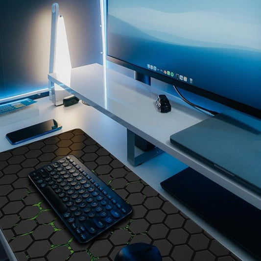 Rubprint Desk Mat – black hexagon desk mat with green accents under a keyboard and mouse, near a lit monitor and desk lamp