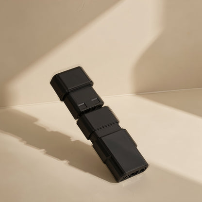 Airspin – Black connector pieces stacked in a staggered line, cast in angled sunlight on a cream surface
