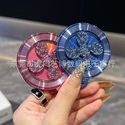 Swivelnest – Pink and blue metallic clover-spinner ring stands held together in a hand with glittery nails