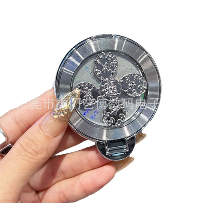 Swivelnest Rotating Phone Stand – silver clover-spinner ring stand with studded petals and fold-out tab, held between fingers