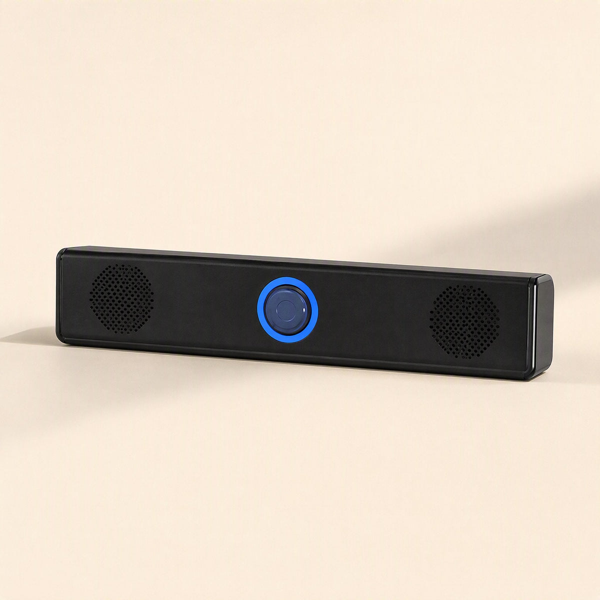 Soundbit – Black mini soundbar with a lit blue ring knob and two round speaker grilles, front view on a beige surface
