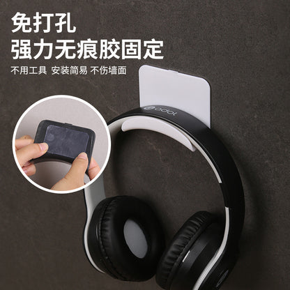 Earhook – Hand pressing the adhesive back of the white no-drill stand, with headphones hanging from it on a wall