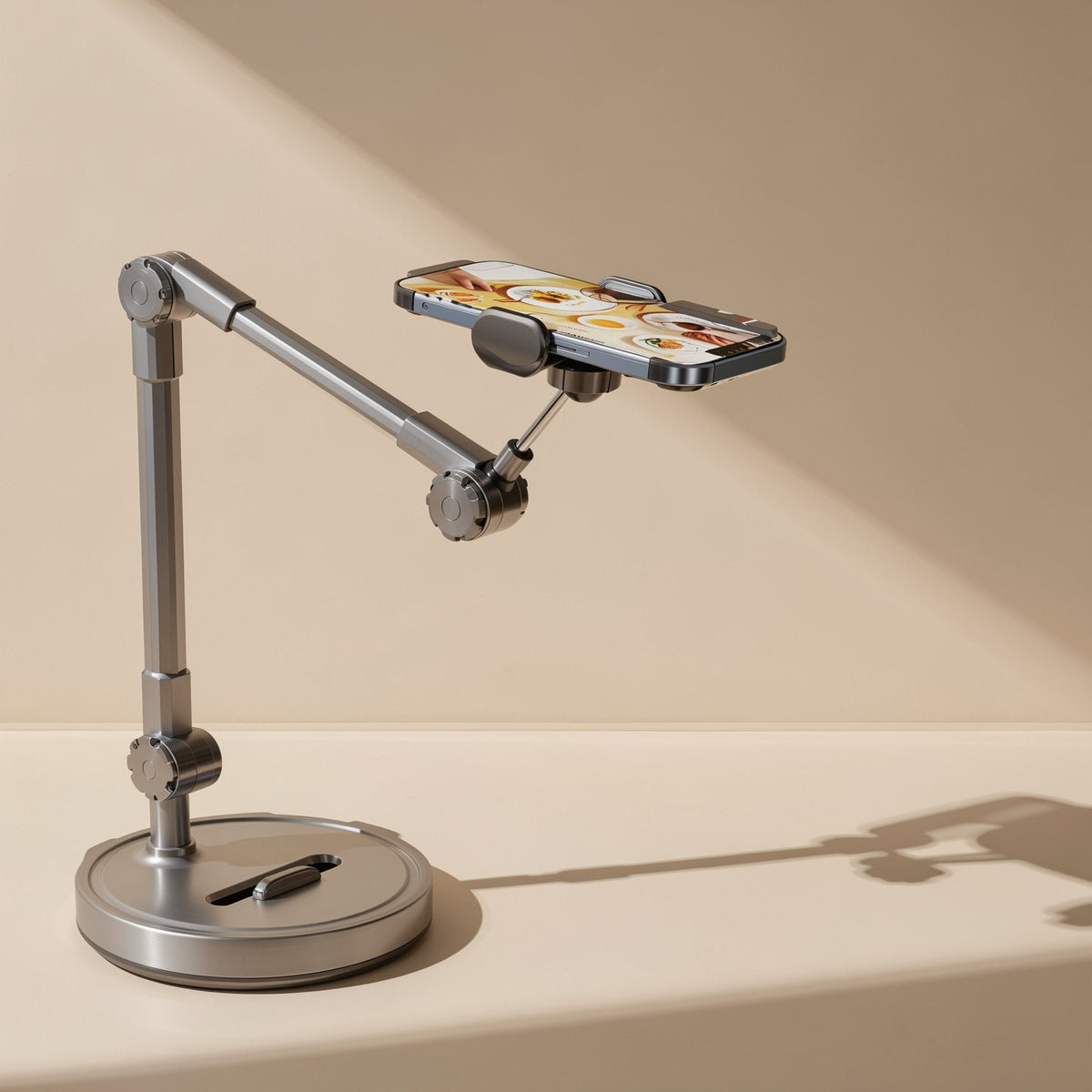 Hoverhold Overhead Phone Stand in brushed alloy with a phone held above a round base on a beige tabletop