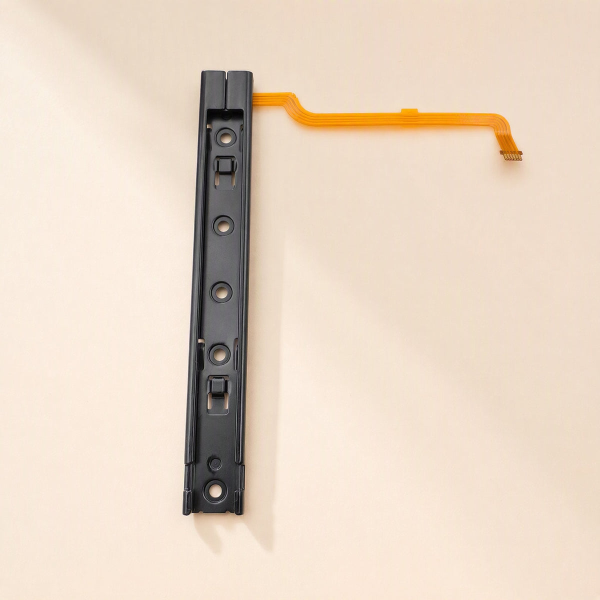 Railglide – Single black slide rail from above with four screw holes and a long orange flex cable extending right