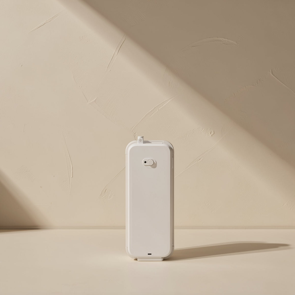 Stickcord – Back of a white rectangular device standing upright on a beige surface against a plaster wall
